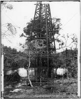 Partial view of derrick by small pool with trees