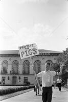 Photograph of Alpha Phi Omega member with "Protest the Pigs" sign