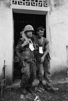Photograph of a U.S. Marine helping a wounded Marine out of a church in Vietnam, 1967