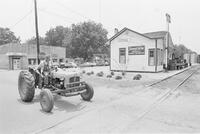 Photograph of a man on a tractor driving past Jimmy Carter's presidential campaign headquarters in Plains, Georgia, June 12, 1976