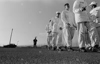 Photograph of a line of prisoners and a guard in the background, September 1995