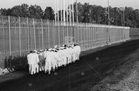 Photograph of a line of prisoners walking near a fence, September 1995