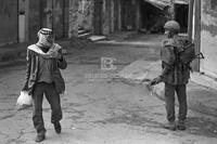 Photograph of a Palestinian man walking by an Israeli soldier