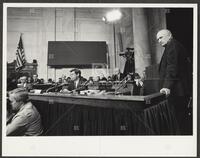 Black and white photograph of Jack Brooks, standing with hand on desk, during the Iran-Contra trials, 1987