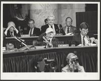 Black and white photograph of Jack Brooks shading his eyes, representatives behind him, during the Iran-Contra trials, 1987