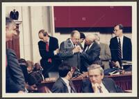 Color photograph of Jack Brooks placing hand on the suit of fellow representative during the Iran-Contra trials, July 1987