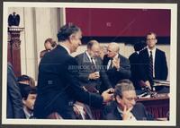 Color photograph of Jack Brooks gesturing and speaking with a fellow representative during the Iran-Contra trials, July 1987