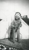 [Unidentified man wearing native American headdress and holding drum]